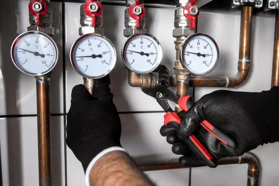Technicien en gants noirs effectuant une maintenance sur installation de chauffage avec cl&eacute; &agrave; molette