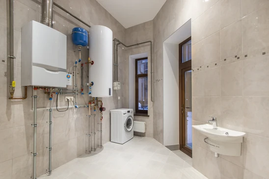 Salle technique moderne avec chaudi&egrave;re murale blanche, ballon d'eau chaude vertical, syst&egrave;me de plomberie apparent avec vannes et raccords color&eacute;s
