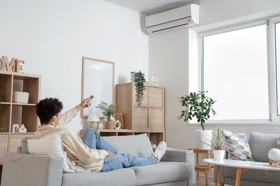 Technicien en combinaison de travail effectuant la maintenance d'une unit&eacute; de climatisation murale dans un environnement int&eacute;rieur