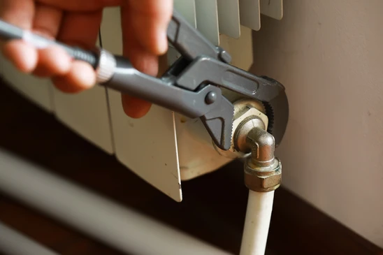 Technicien en tenue professionnelle Riemer diagnostiquant un problème de chauffage en intérieur résidentiel : il utilise un appareil de diagnostic thermique ou un multimètre pour tester une installation défaillante, peut-être un radiateur ou un système qui ne fonctionne pas correctement. La scène montre l'expertise technique et la réactivité de dépannage, dans un contexte urgent mais maîtrisé. L'environnement doit être un domicile client, l'équipement défaillant clairement visible, mettant l'accent sur le diagnostic professionnel plutôt que sur l'installation ou la maintenance préventive.