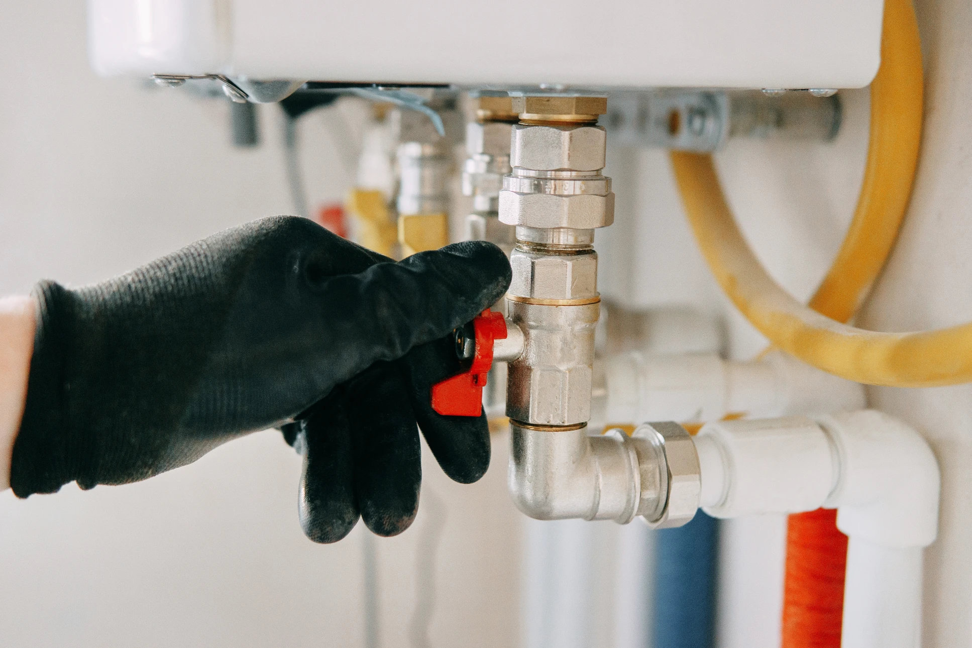 Technicien en combinaison bleue et gants rouges effectuant la maintenance d'une chaudière murale dans un local technique